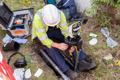 Technician repairing equipment in a trench, surrounded by tools and materials. The image highlights maintenance work on utility infrastructure.