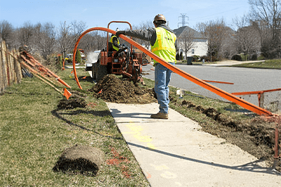 Two installers work together to install conduit for fiber optic cable.
